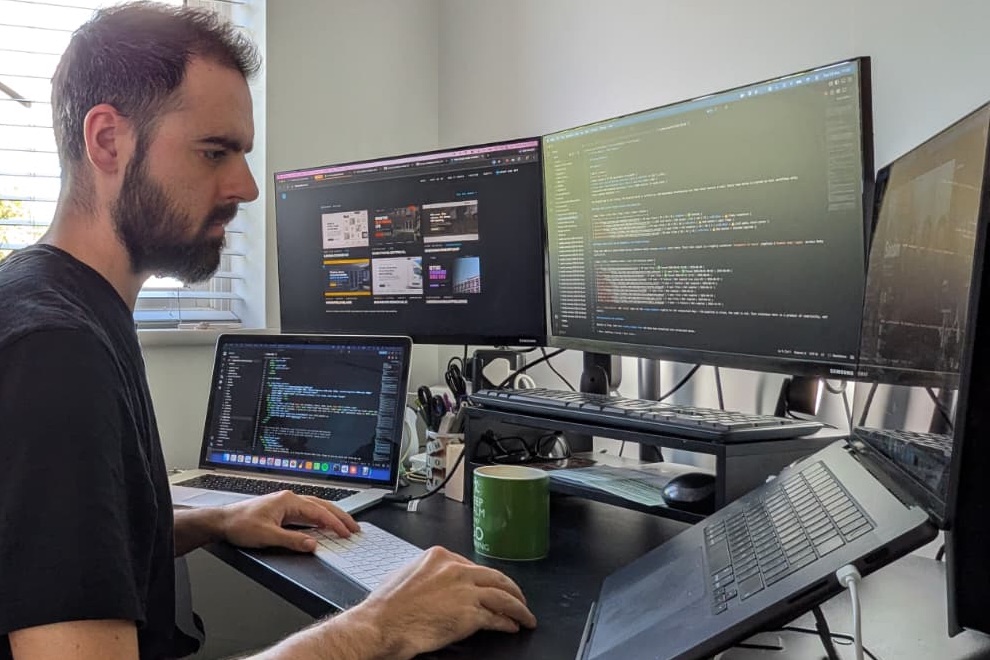 Dan at his desk in Bedford, working on a client's website across two monitors and a laptop